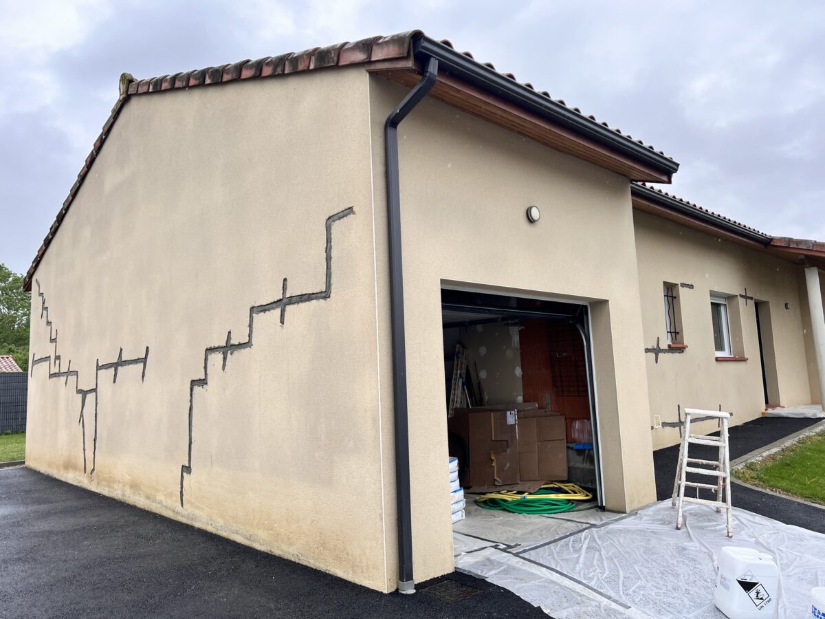 Façade de maison avec fissures sur l'espace façades, réparation en cours.