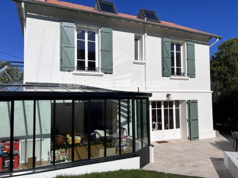 Façade de maison rénovée avec volets verts et véranda par Espace Façades