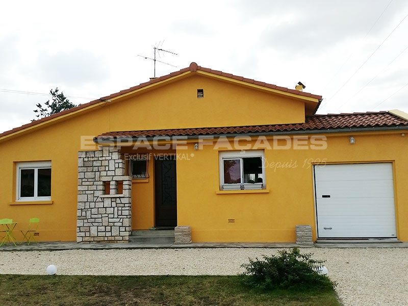 Maison jaune avec porte de garage et entrée en pierre.